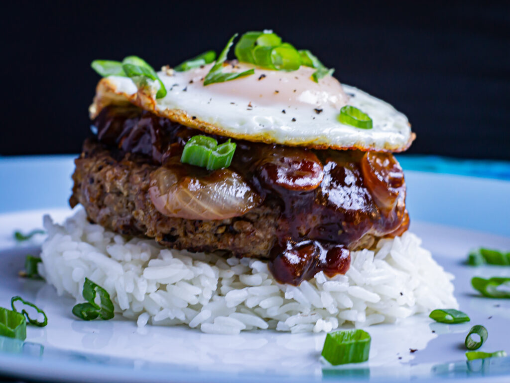 Hawaiian Loco Moco vertical. Rice topped with burger, gravy, and egg